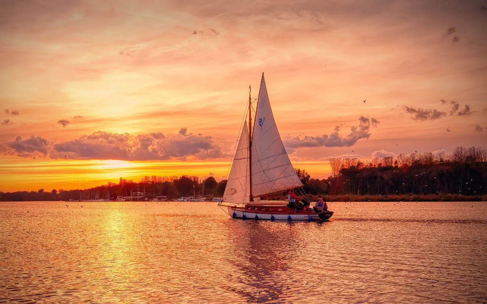 A serene sailboat glides across calm waters at sunset on the Norfolk Broads